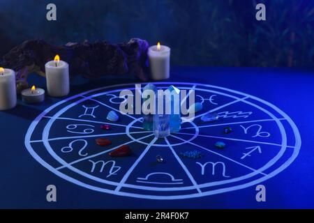 Pietre naturali per i segni zodiacali, grafico astrologico disegnato e candele brucianti su tavola blu scuro Foto Stock