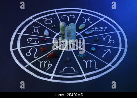 Pietre naturali per segni zodiacali e grafico astrologico disegnato su sfondo blu scuro Foto Stock