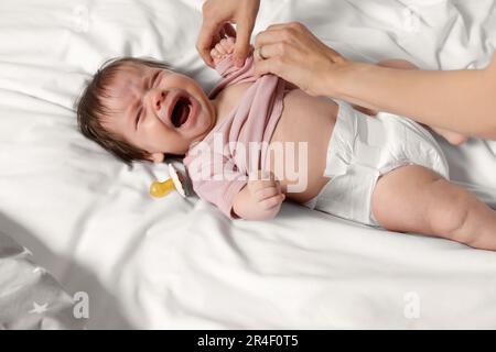 Madre che mette i vestiti sulla figlia piangente sul letto, primo piano Foto Stock