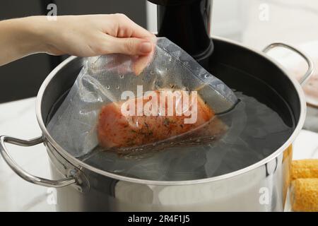 Donna che mette la carne sottovuoto impaccata in pentola con cucina sous vide, primo piano. Circolatore a immersione termica Foto Stock