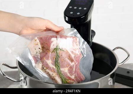 Donna che mette la carne sottovuoto impaccata in pentola con cucina sous vide, primo piano. Circolatore a immersione termica Foto Stock