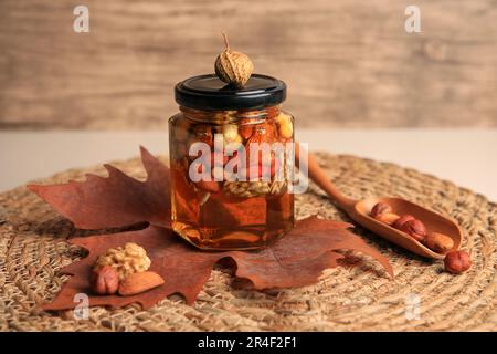 Noci diverse con miele in vaso, cucchiaio e foglia secca sul tavolo Foto Stock