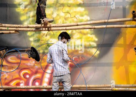 Uomo in piedi su impalcature di bambù utilizzando una pistola ad aria spray per dipingere una foto di hanuman il dio indù sul ponte janaki setu a rishikesh India Foto Stock