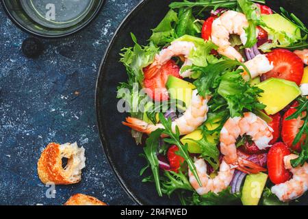 Insalata di yummy con fragole fresche, gamberi, rucola, avocado e cipolla rossa, tavolo in pietra blu. Piatto fresco utile per un'alimentazione sana Foto Stock