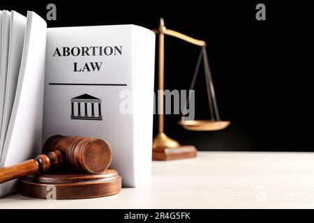 Libro di legge sull'aborto, gavel e scale di giustizia su tavola bianca su sfondo nero Foto Stock