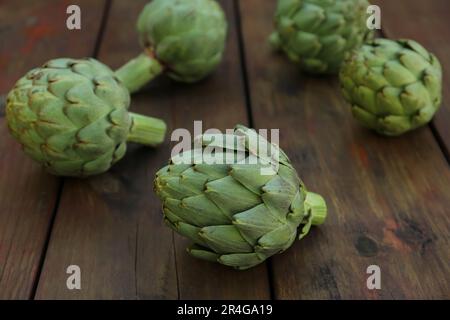 Carciofi freschi interi crudi su tavola di legno, primo piano Foto Stock