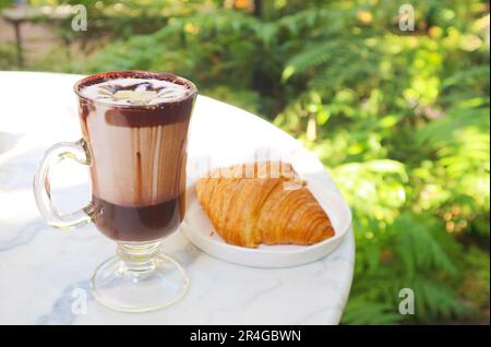 Bicchiere di cioccolata calda con un croissant francese sul tavolo bianco Foto Stock