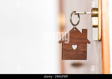 Portachiavi in legno a forma di casa con un foro centrale a forma di cuore appeso ad una chiave inserita nella serratura di una porta anteriore di una casa. Foto Stock