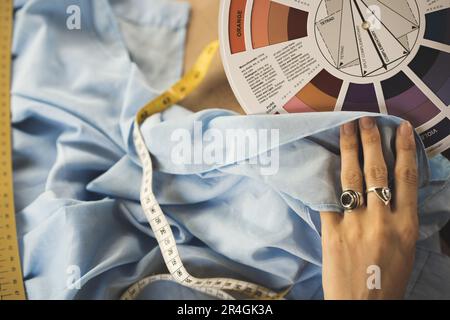 Una stilista di moda femminile tiene campioni di fiori nelle sue mani, scegliendo un tessuto di tonalità blu di tessuti sul posto di lavoro, un comò o su misura, ha Foto Stock