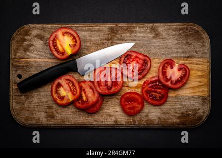 Pomodori ciliegini a fette con coltello su tavola di legno sullo sfondo con spazio di copyspace. Verdure al pomodoro sane e biologiche per una vista dall'alto della bruschetta Foto Stock