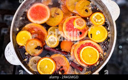 Vite speziata tritata con arance in vaso nel mercato alimentare di strada. Bevanda alcolica calda colorata al closeup del festival della fiera all'aperto Foto Stock