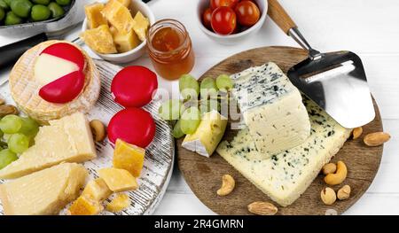 Diversi tipi di formaggio servito con olive verdi, pomodoro e uva per la nutrizione gourmet. Parmigiano e brie biologici con specialità al miele Foto Stock