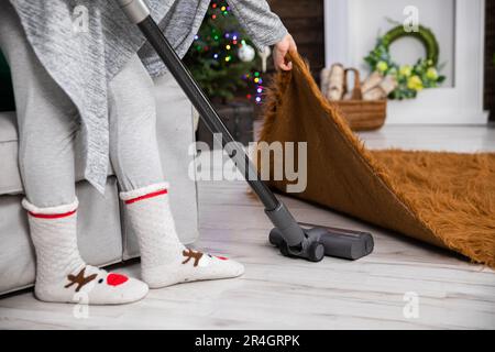 La donna pulisce accuratamente il pavimento mentre aspira, anche sotto il tappeto. Foto Stock