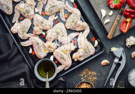 Preparare il cibo con ali di pollo crude e biologiche poste con ingredienti freschi sul vassoio nero Vista dall'alto con primo piano. Foto Stock