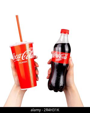 Berlino Germania Maggio 23 2023 bevanda analcolica di Coca Cola in tazza di carta da asporto e in bottiglia trasparente di plastica in mano isolata su bianco. Foto Stock