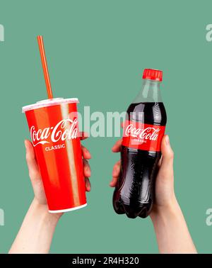 Berlino Germania Maggio 23 2023 bevanda analcolica Coca Cola in tazza di carta da togliere con cannuccia e in bottiglia trasparente di plastica in mano. Foto Stock