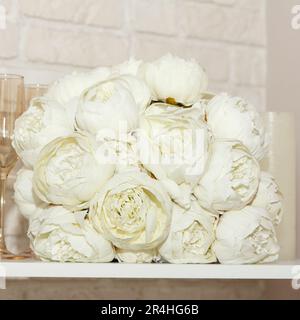 Un bouquet bianco di nozze di peonie, bicchieri e candele bianche si trovano sullo scaffale. Splendido set per sposi. Bellissimo sfondo, piazza. Foto Stock