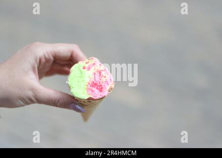 Una donna tiene un cono gelato in entrambe le mani. Il gelato è morso. Primo piano. Foto Stock
