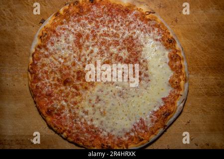 Pizza appena sfornata con salsa di pomodoro e formaggio su un tagliere di legno Foto Stock