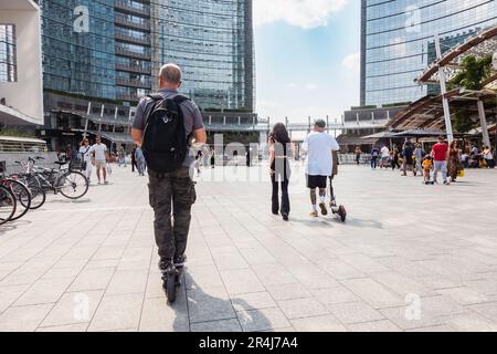 Milano, uomo a cavallo scooter elettrico. Persone con scooter elettrici in piazza Gae Aulenti. Zona pedonale nella moderna piazza di Milano. Italia Foto Stock