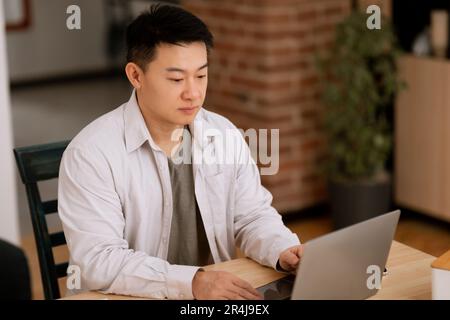 Uomo asiatico di mezza età concentrato che utilizza il notebook, lavora online da casa, ha riunioni di lavoro online, spazio copia Foto Stock