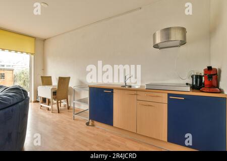 una cucina e soggiorno in un appartamento con pavimento in legno, armadi blu, pareti bianche e pareti con accento giallo Foto Stock