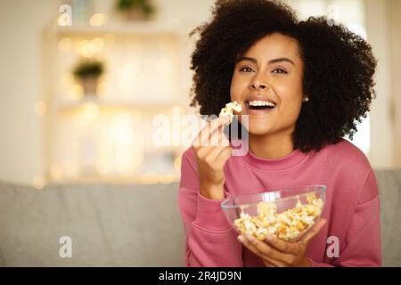 Allegro giovane signora nera mangiare Popcorn guardare film a casa Foto Stock