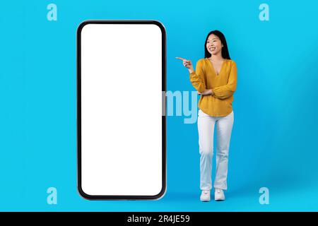 Bella donna asiatica skinny che indica uno smartphone enorme Foto Stock