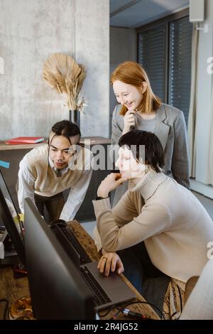 Donna d'affari sorridente con programmatori che guardano il computer in ufficio Foto Stock