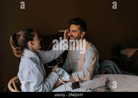 Persona non binaria che applica il make-up al ragazzo mentre si siede a casa Foto Stock