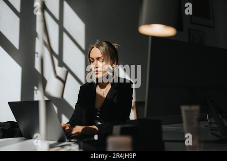 Giovane donna d'affari che lavora su un computer portatile seduto in ufficio Foto Stock