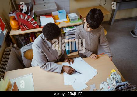 Vista ad angolo alto dell'insegnante che aiuta il ragazzo con il diagramma alla scrivania in aula Foto Stock