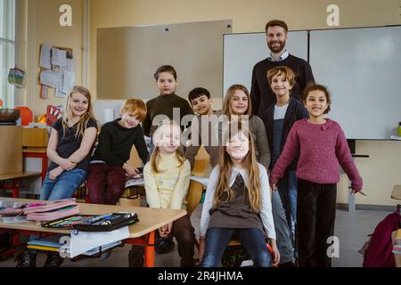 Ritratto dell'insegnante sorridente e delle ragazze e dei ragazzi contro la lavagna in classe Foto Stock