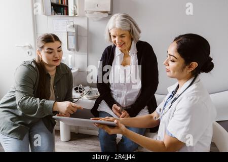 Medico che discute con la donna anziana e la figlia sopra il PC del tablet in clinica Foto Stock