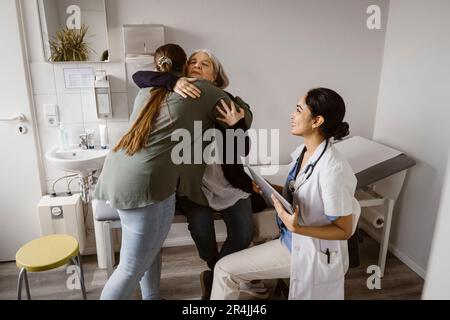 Figlia che abbraccia la madre seduta a letto da una figlia in clinica Foto Stock