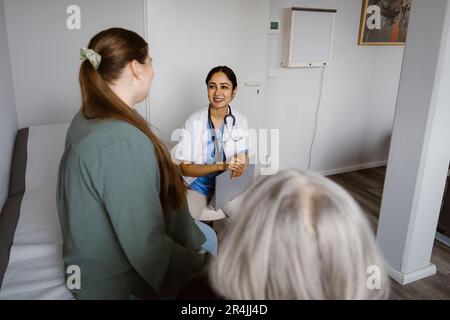 Medico sorridente che discute con il paziente seduto in sala di consulenza Foto Stock