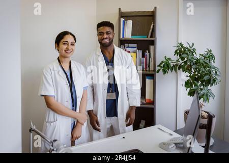Ritratto di operatori sanitari sicuri di sesso maschile e femminile in piedi alla scrivania presso la clinica Foto Stock