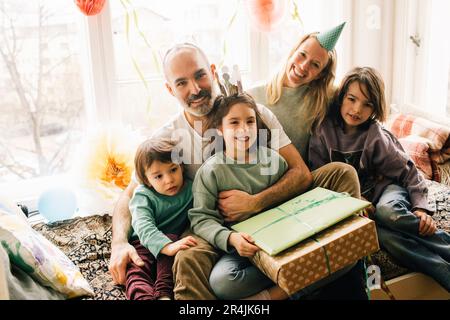 Ritratto di felice compleanno ragazza seduta con regali e la famiglia su alcova posto a casa Foto Stock