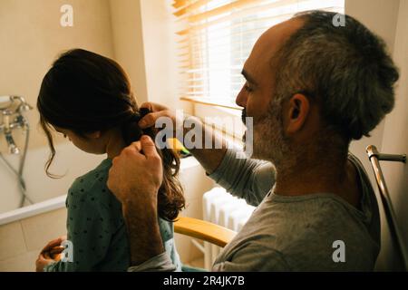 Padre intrecciando i capelli della figlia in bagno Foto Stock