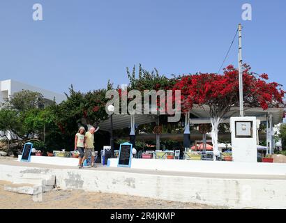 Coppie mature camminano davanti a una Taverna sulla spiaggia, con bouganvillea, Skala, Agistri Island, vicino ad Atene. Gruppo dell'isola Saronica. Preso il 2023 maggio. cym Foto Stock