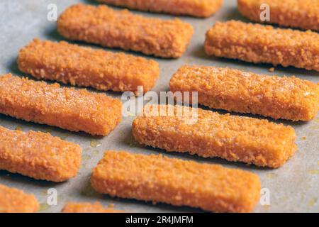 Molti bastoncini di pesce pronti per friggere su carta speciale. Concetto di cottura per friggere le dita di pesce nel forno. Vista laterale. Foto Stock