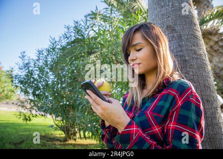 Una ragazza mangia una mela e usa il suo smartphone, stile di vita sano Foto Stock