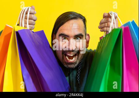 Primo piano di un uomo che tiene borse shopping colorate su sfondo giallo Foto Stock