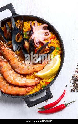 Piatto classico della Spagna, paella di pesce in padella tradizionale su sfondo bianco, vista dall'alto. Paella spagnola con gamberetti, pinze, cozze, piselli verdi e. Foto Stock