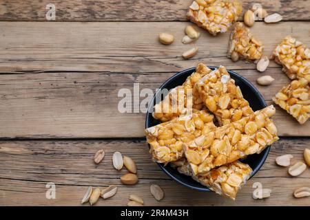 Deliziose barrette kozinaki di arachidi in ciotola su tavolo di legno, piatto. Spazio per il testo Foto Stock