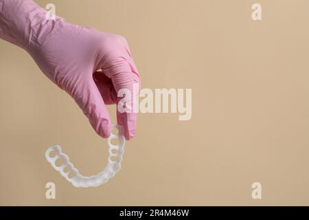 Correzione del morso. Dentista in guanto medico che tiene la protezione della bocca su sfondo beige, primo piano. Spazio per il testo Foto Stock