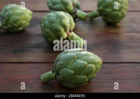 Carciofi freschi interi crudi su tavola di legno, primo piano Foto Stock