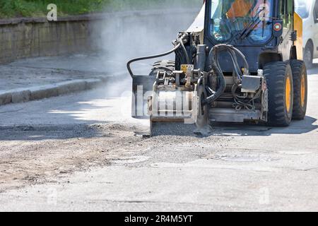 Un trattore stradale da costruzione con un potente attacco di un dispositivo di fresatura attaccato rimuove uno strato di asfalto vecchio sulla carreggiata. Foto Stock