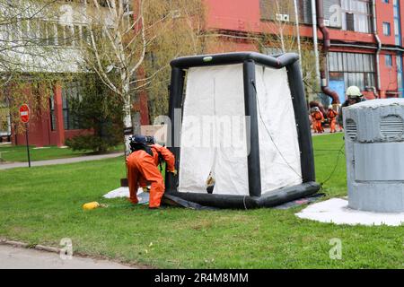 Un pompiere professionale in una speciale tuta ignifuga arancione si prepara ad assemblare una tenda ad ossigeno bianco per salvare le persone in una raffineria chimica, petrolifera, Foto Stock