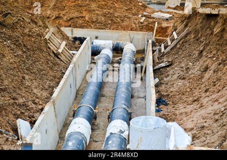 Grandi tubi in metallo nero e plastica per acqua calda e fredda in un cantiere durante una riparazione in un nuovo quartiere sotto terra. Foto Stock